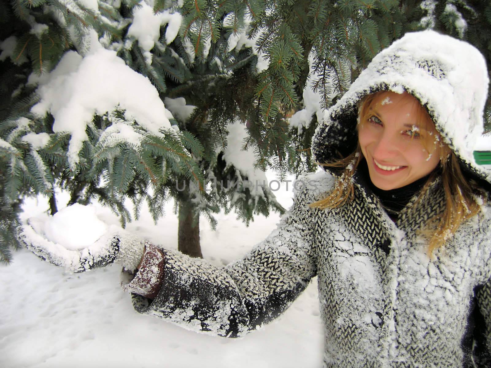 Smiling girl on snowy fir background holding snowball
