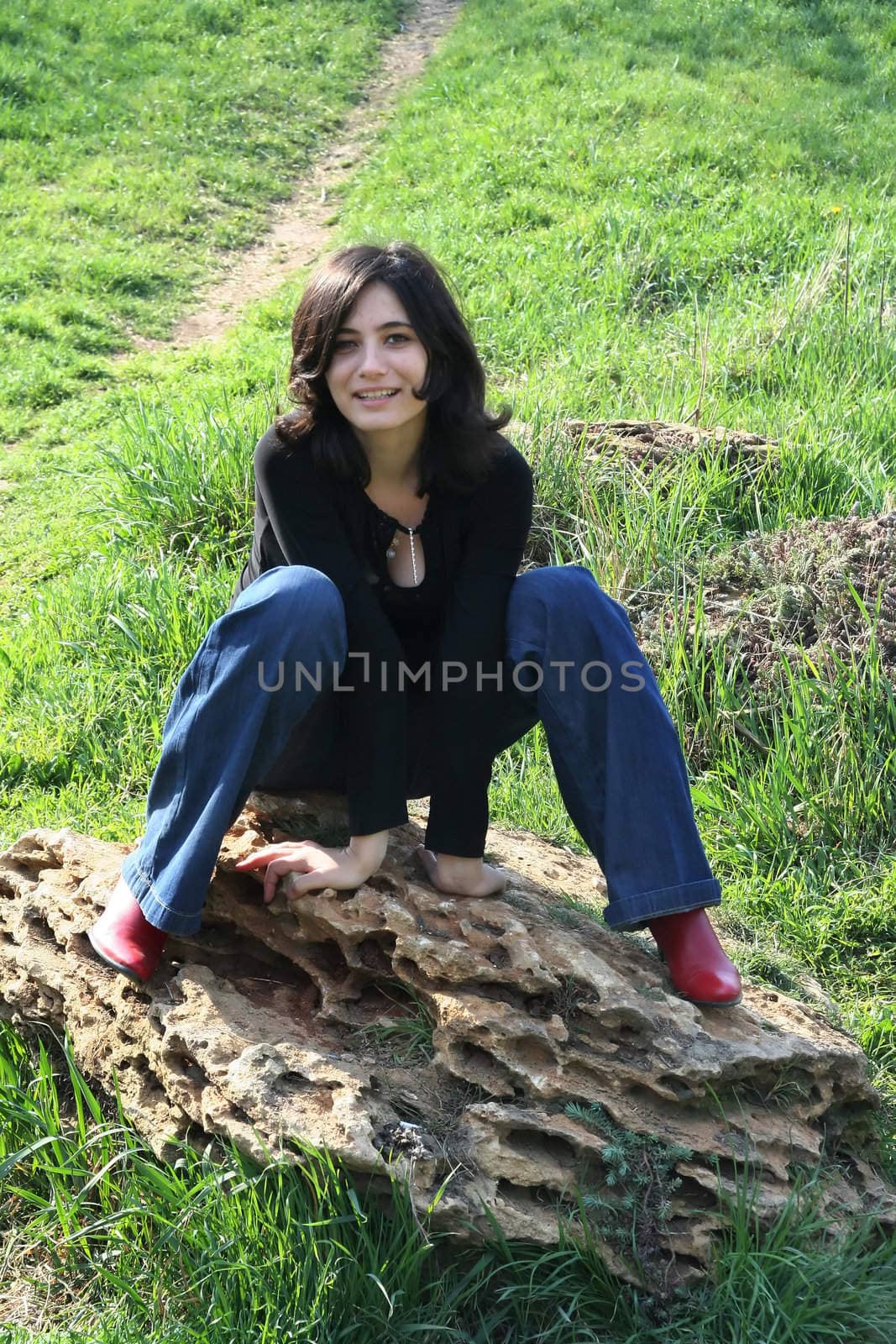 The cheerful girl sits on a stone