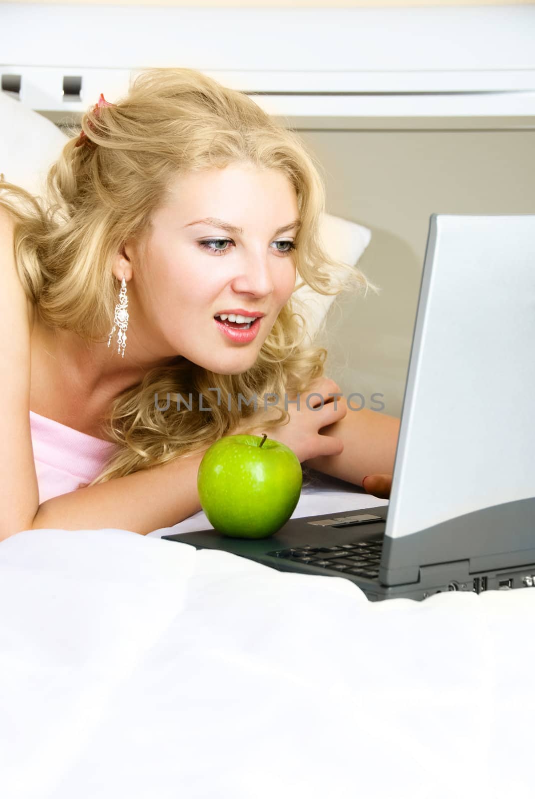 beautiful girl at home on the bed using a laptop and eating a green apple