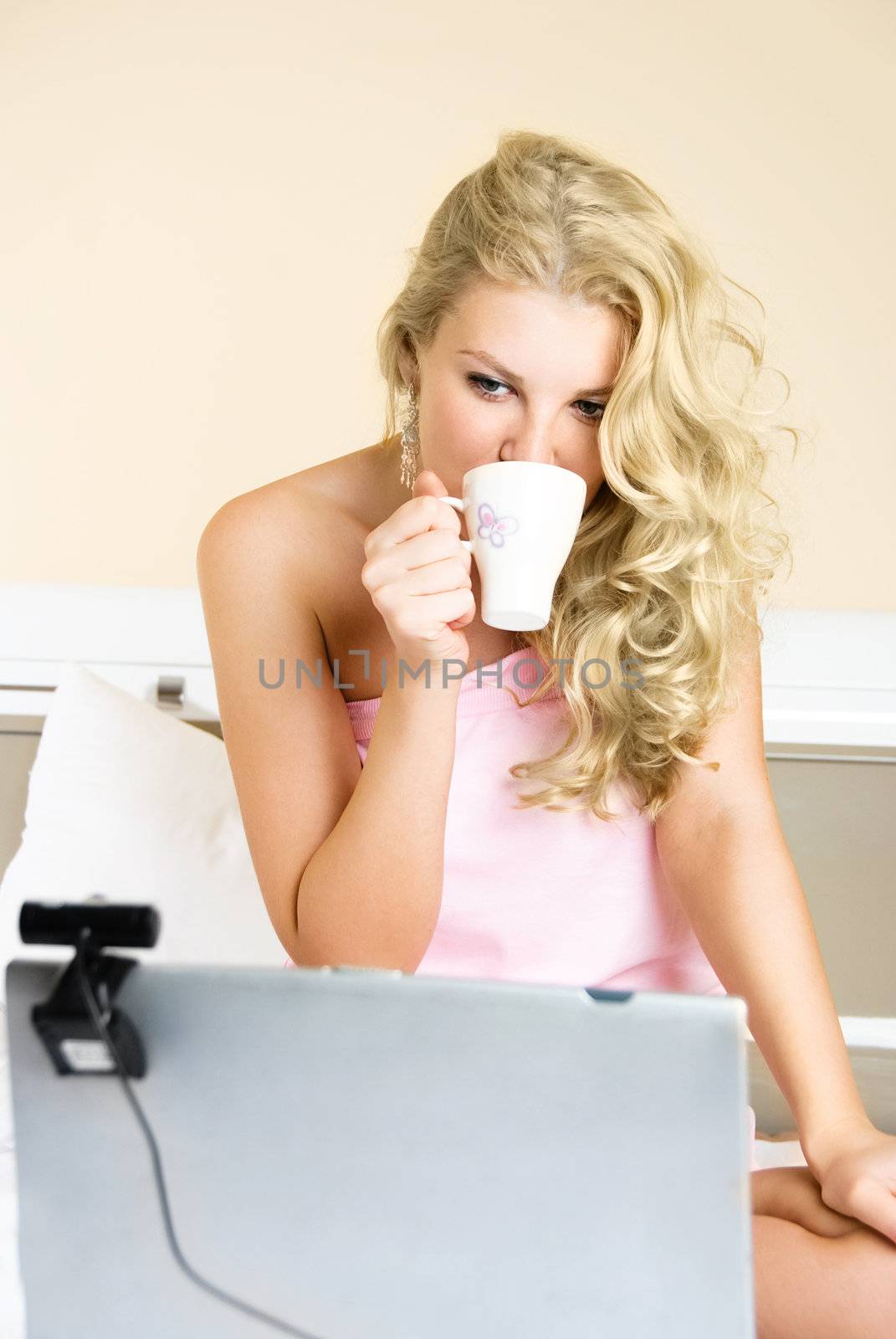 beautiful blond girl at home communicating through the Internet using a web camera and drinking coffee