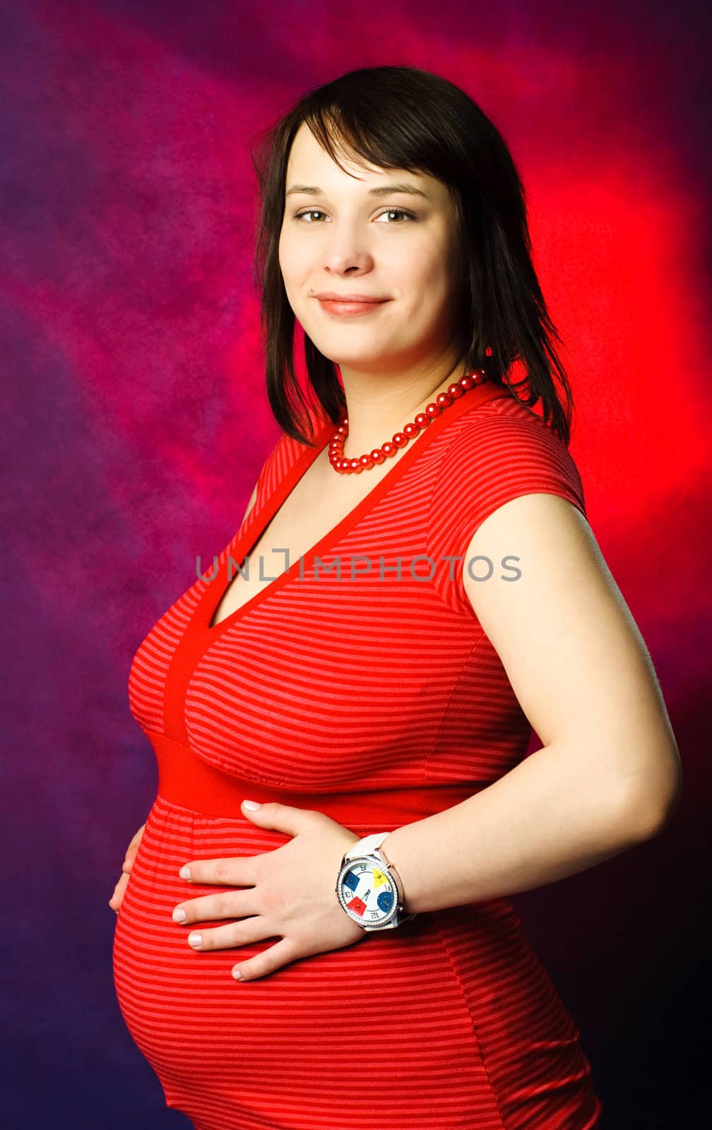 studio portrait of a beautiful young pregnant woman against red background