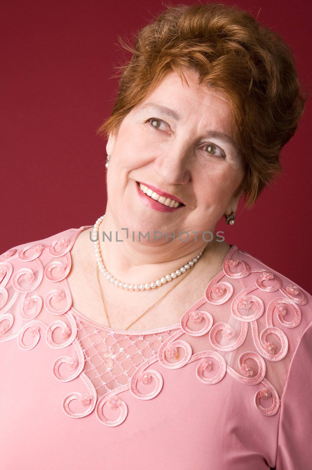 The cheerful elderly woman in a pink dress on a red background.