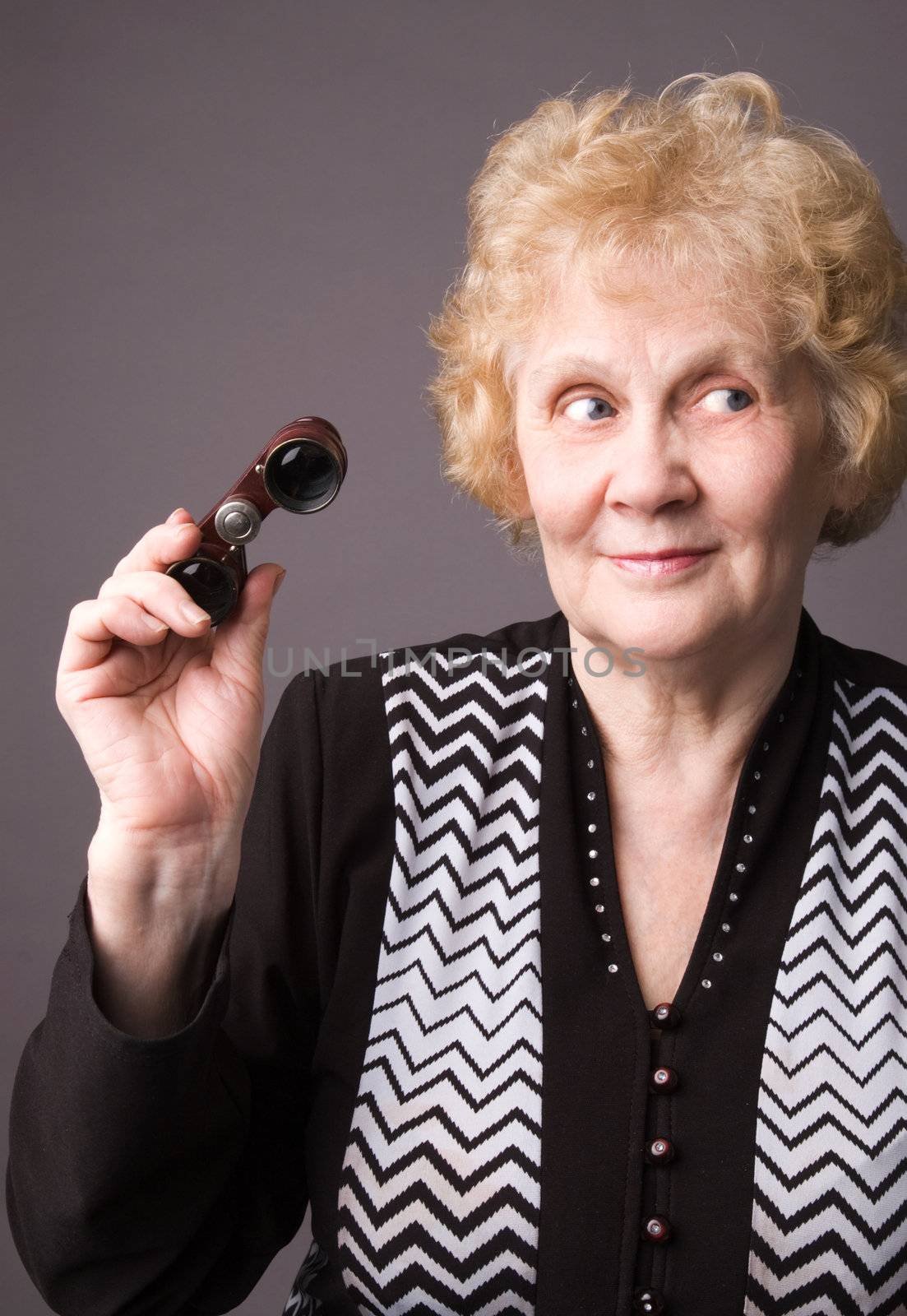The cheerful elderly woman with binocular on a grey background.