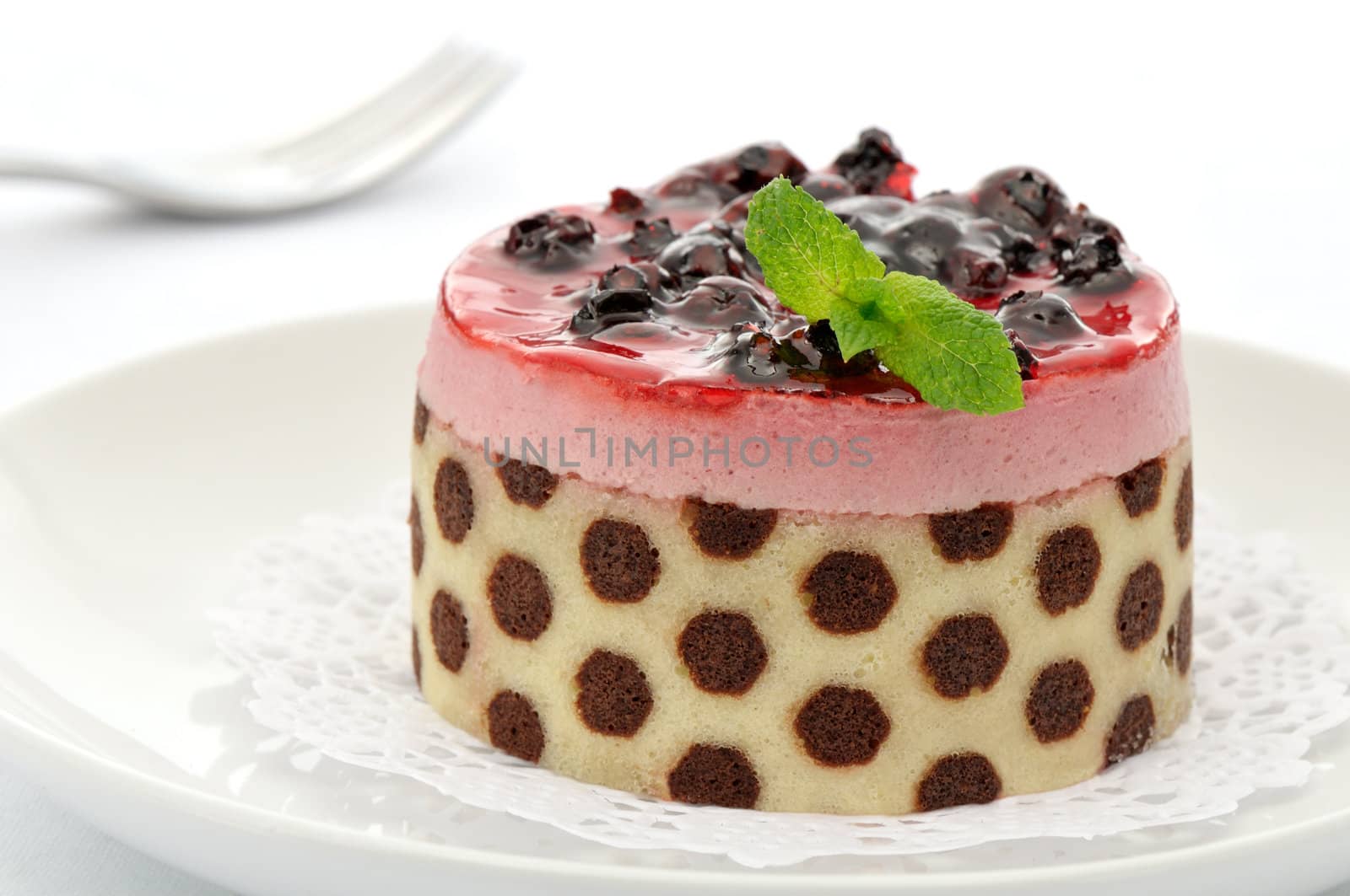 Raspberry mousse cake decorated with blueberries and mint leaves on a white plate
