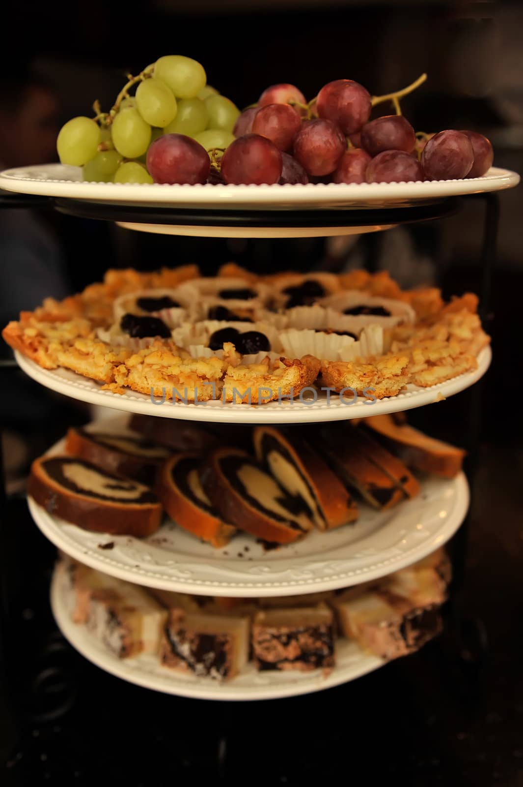 Stack of plates with grapes and various cakes