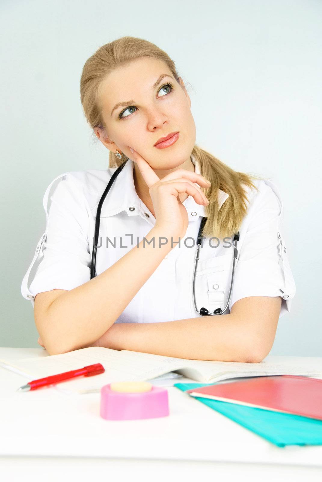 beautiful thoughtful young doctor sitting by the table in the office