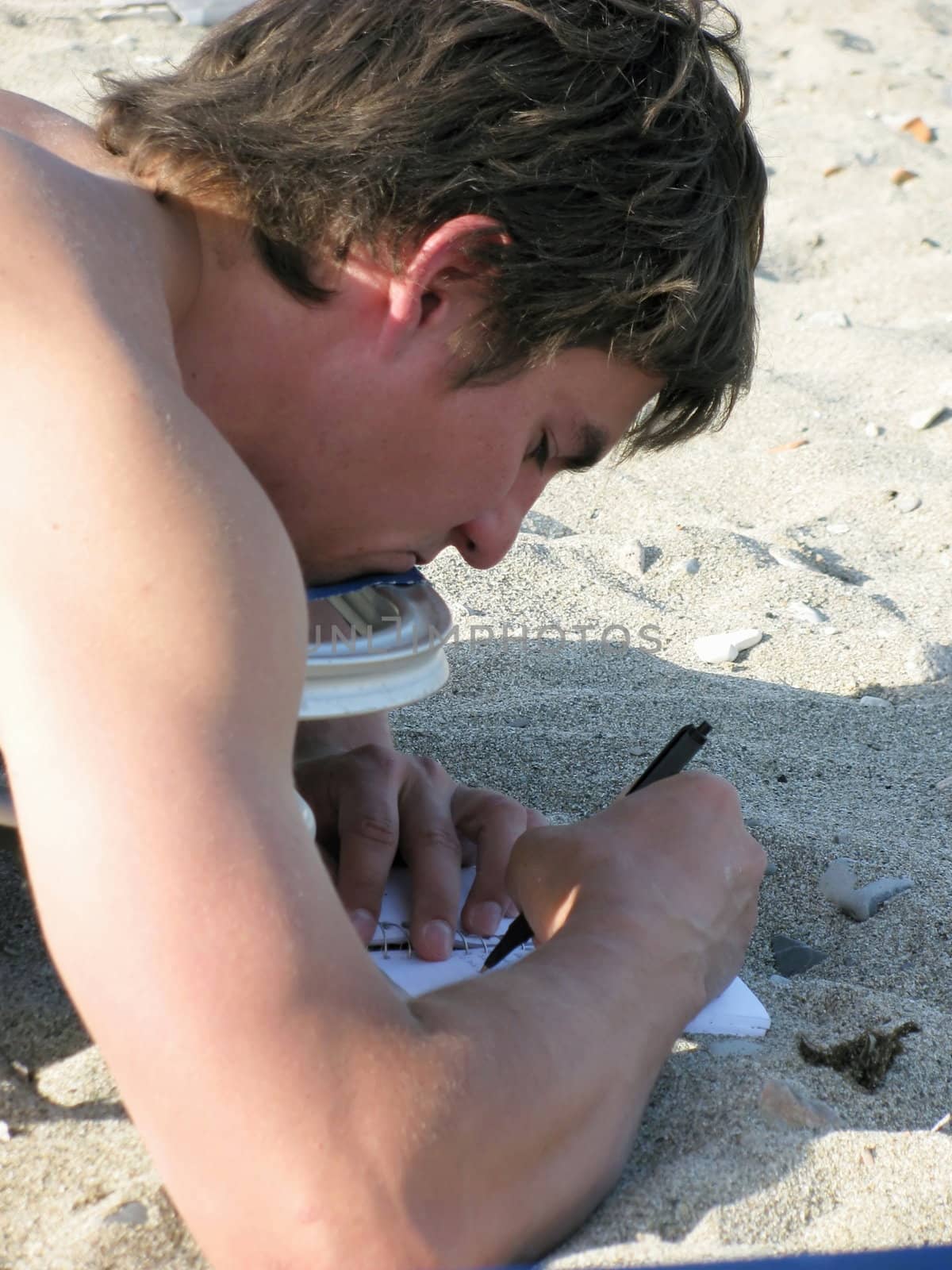 a young man is relaxing on the beach while writing his journal