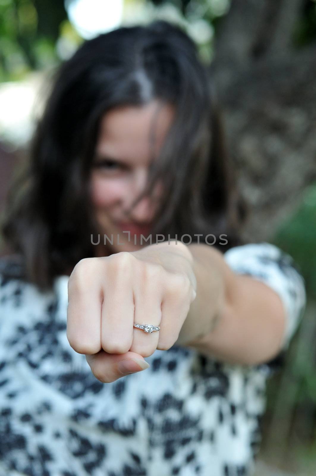 Young, attractive woman punches her hand forward to show off ring.  Selective focus is used.