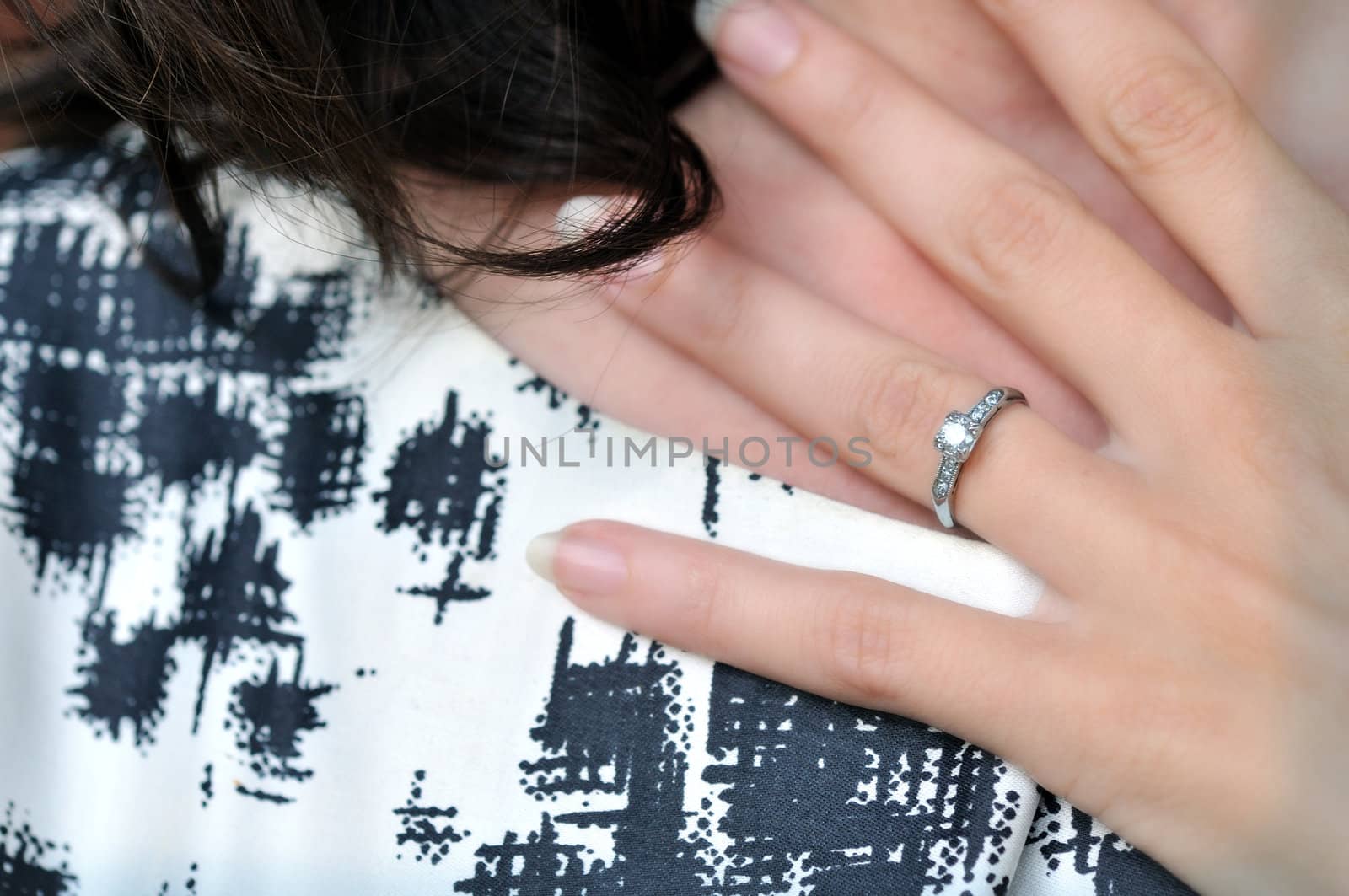 Close-up image of an engagement ring on a woman's hand, held against her neck.