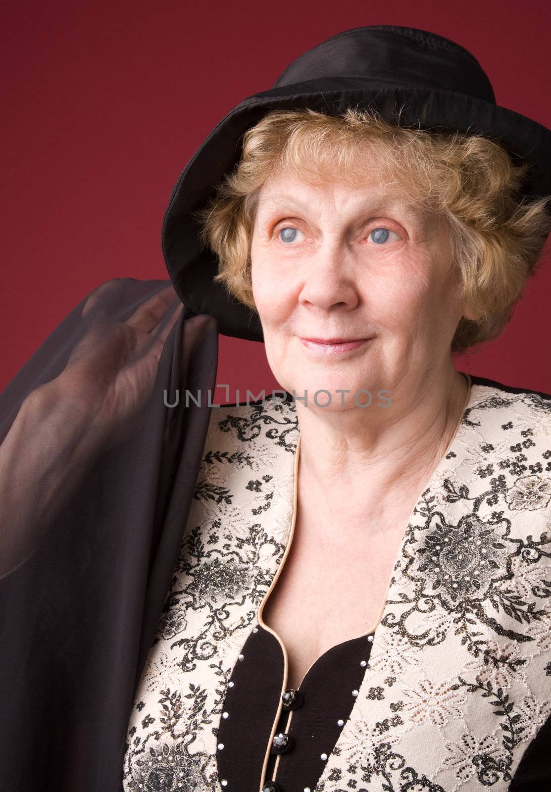 The cheerful elderly woman in hat on a red background.