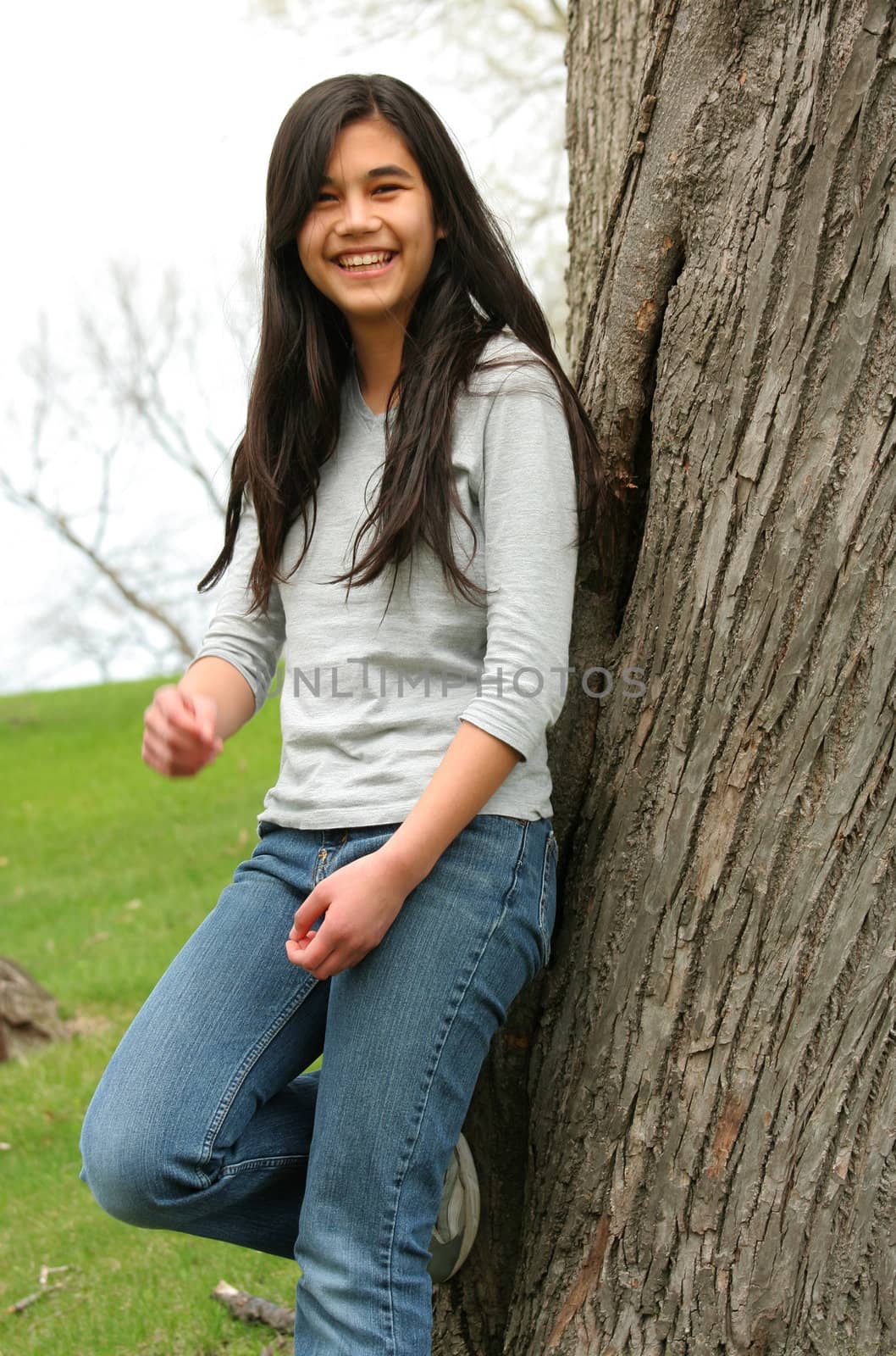 Young teen girl leaning against tree smiling