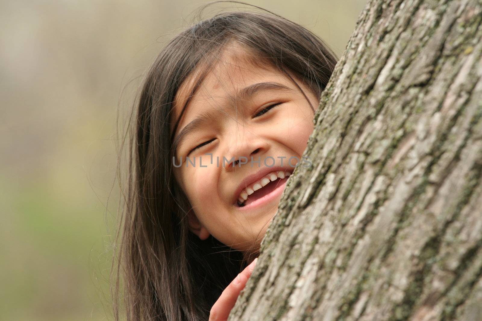 Little girl peeking out from behind a tree