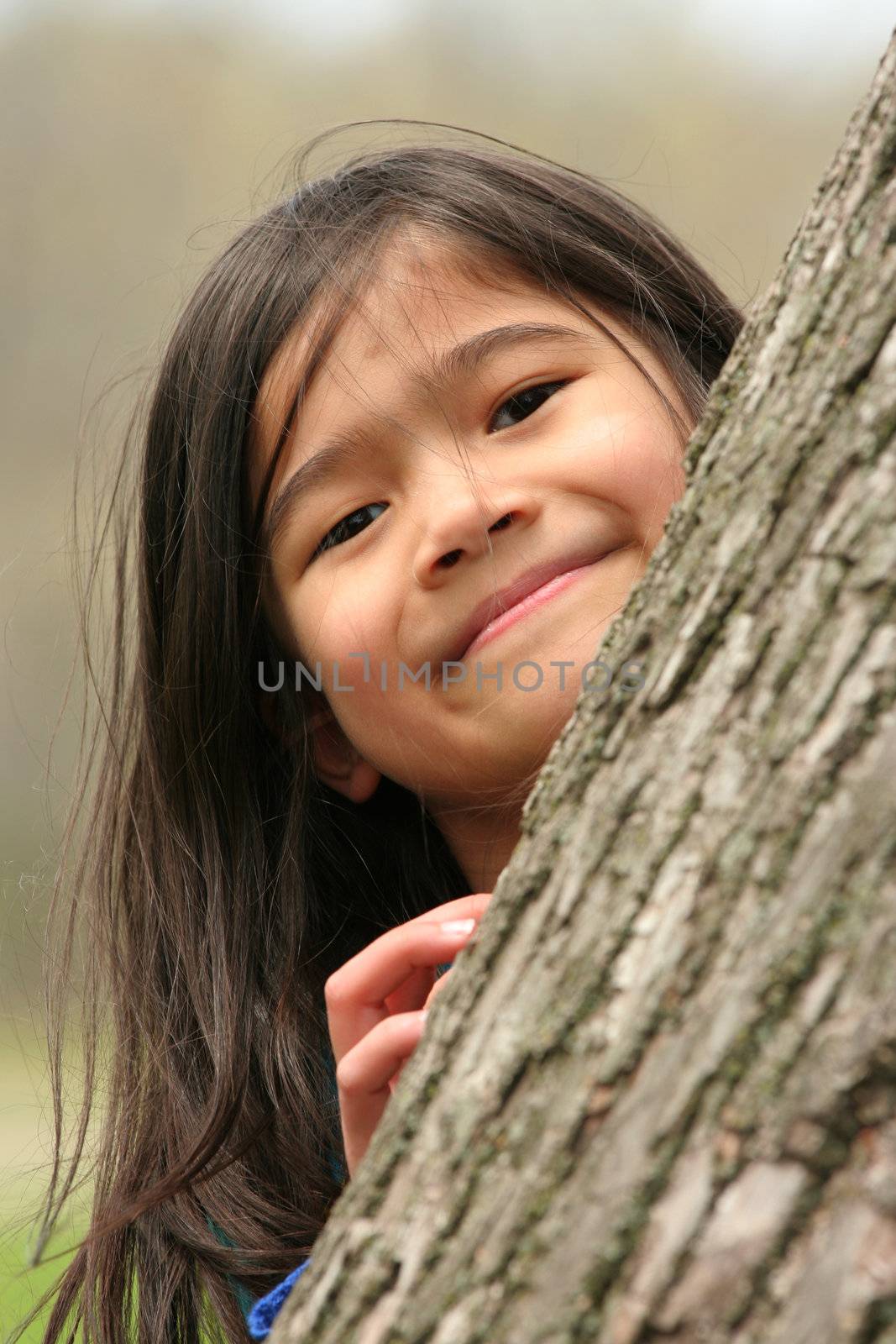 Little girl peeking out from behind a tree