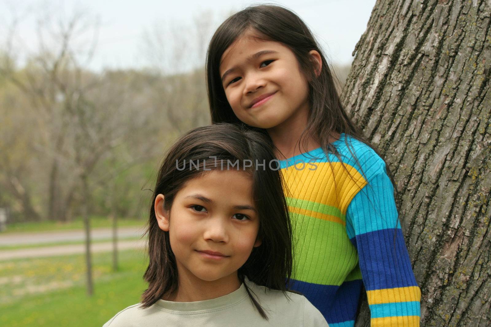 Two little girls standing against tree in spring
