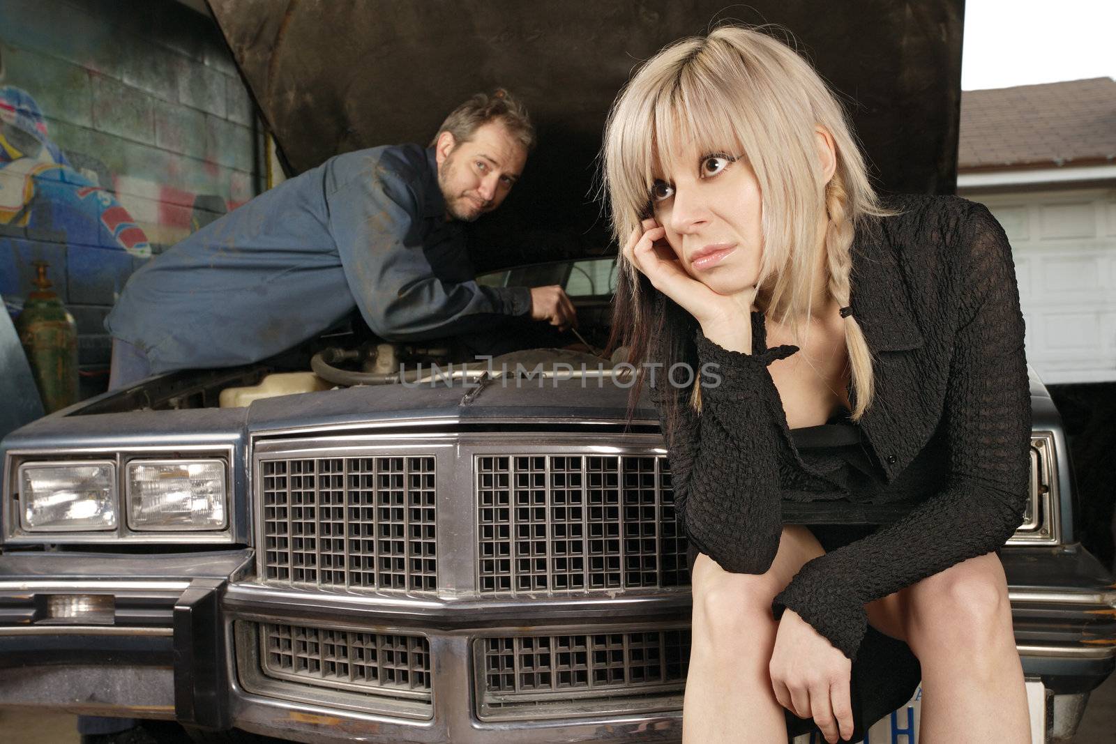 A frustrated blond woman in her thirties waits for a mechanic to fix her old car.
