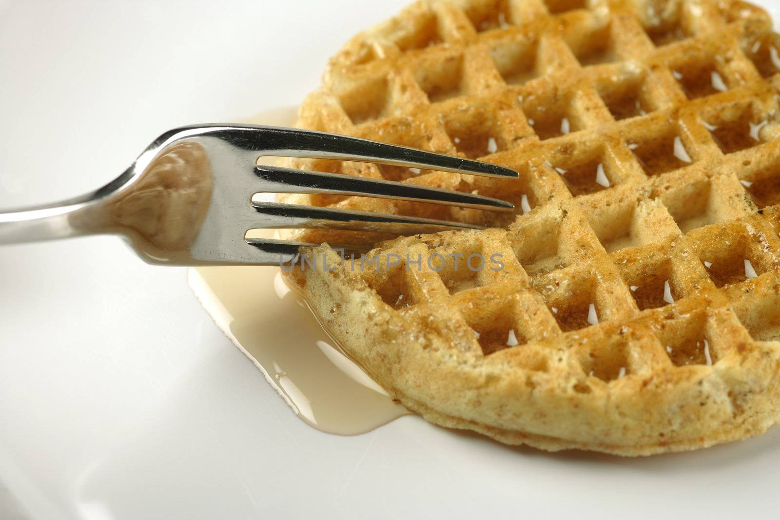 Closeup of a fork cutting through a waffle covered with maple syrup.