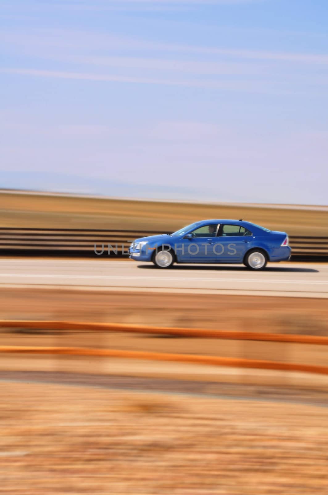 A blue sedan speeds by with the background intentionally blurred due to the movement.