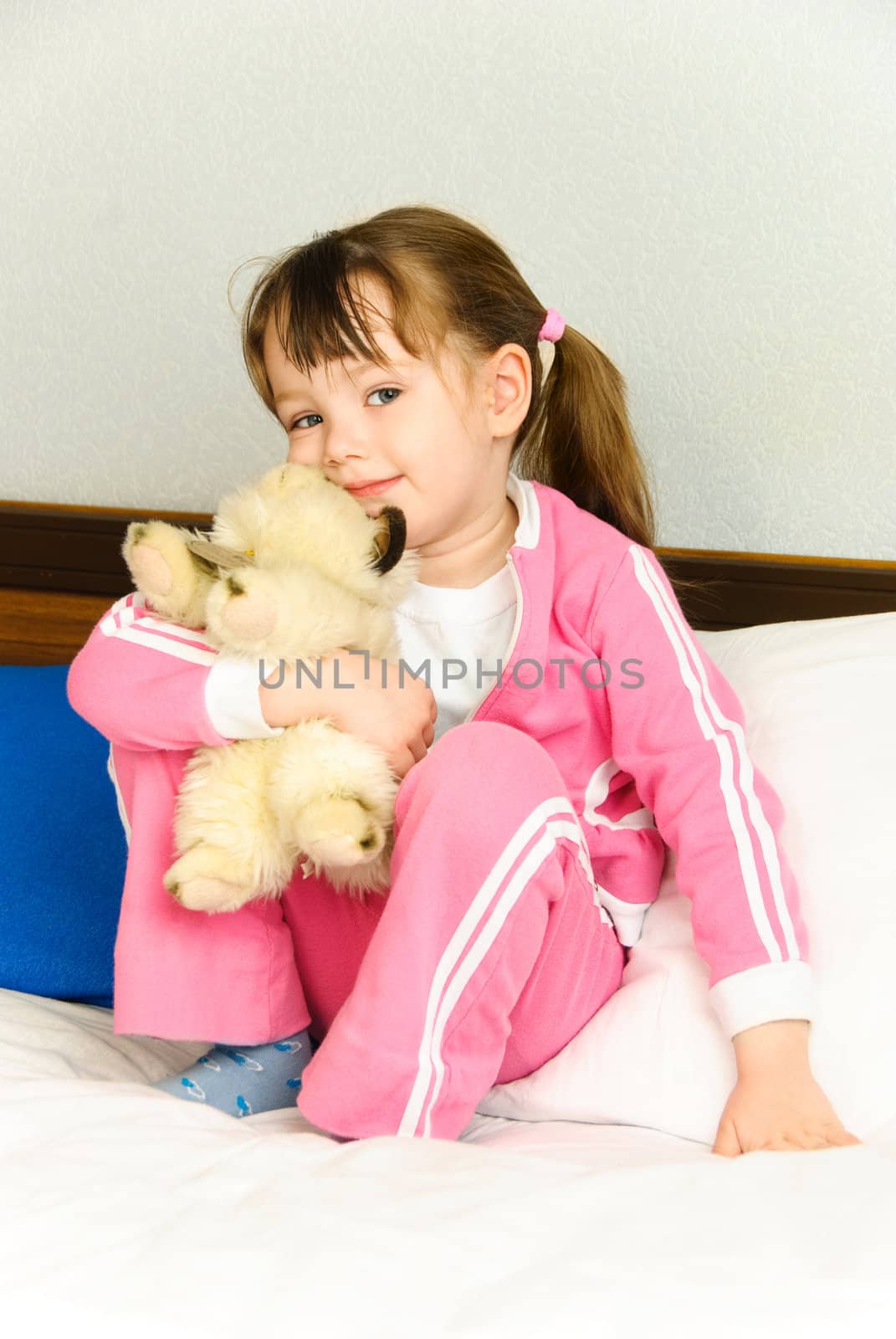 cute little girl with a toy  sitting on the bed at home