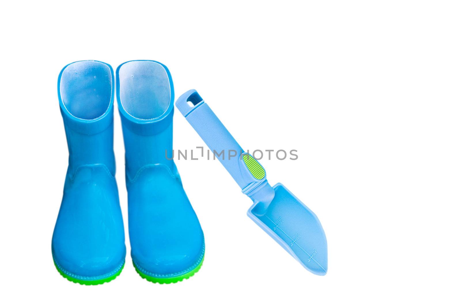 Child's rubber rain boots and garden trowel isolated on white.