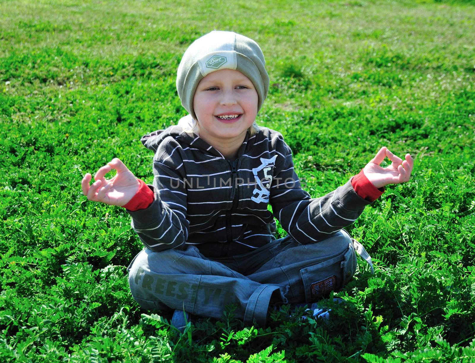 little boy is sitting on the green grass and doing meditation