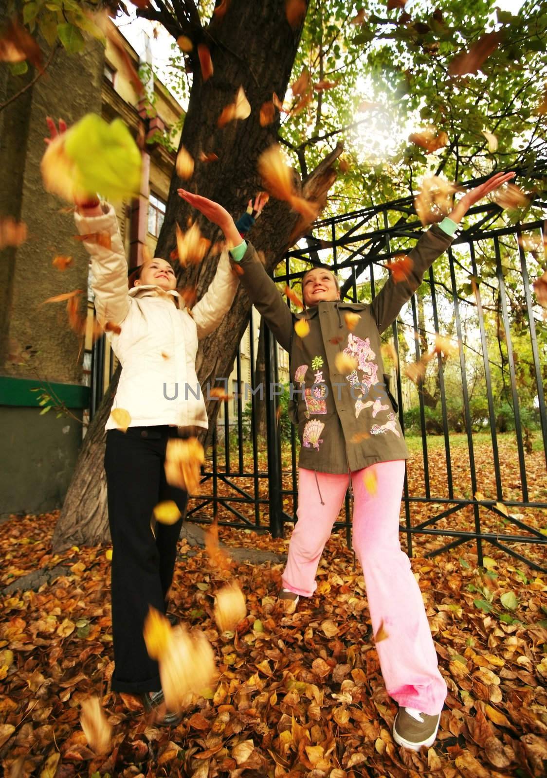 Two girls throw up yellow leaves