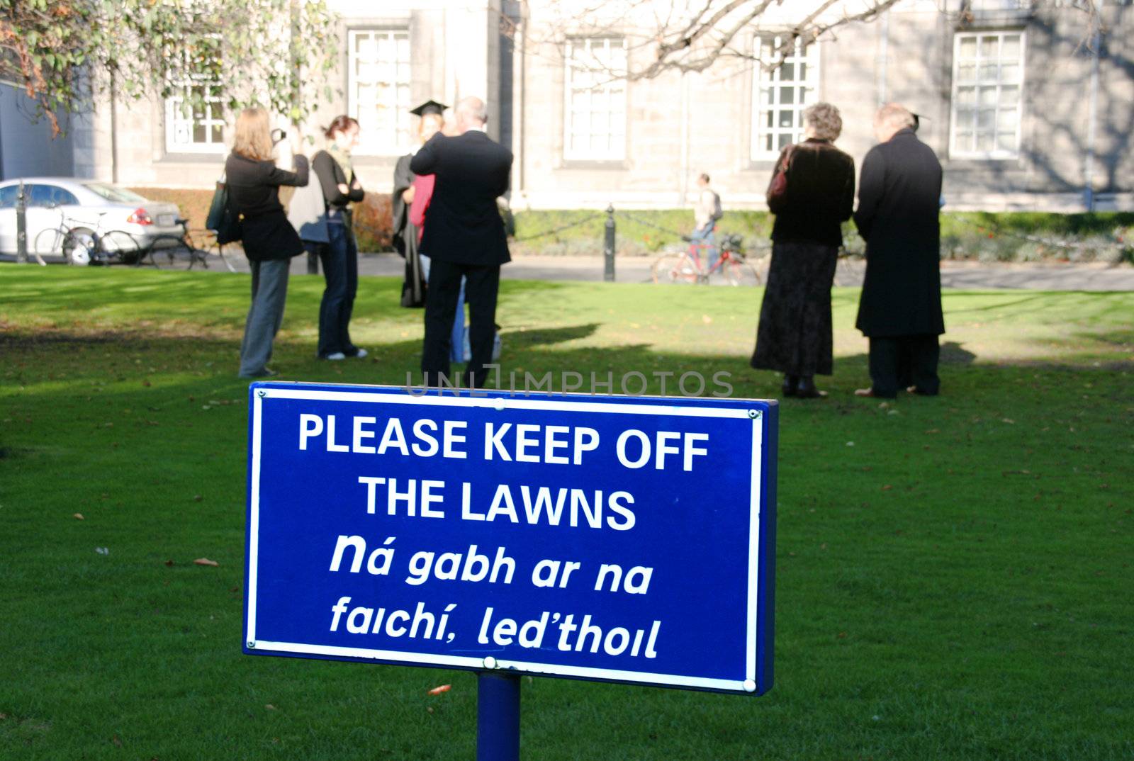 A group of law breaking persons in an Irish city. Very serious crime: not keeping off the lawn. Warning sign in English and Irish.