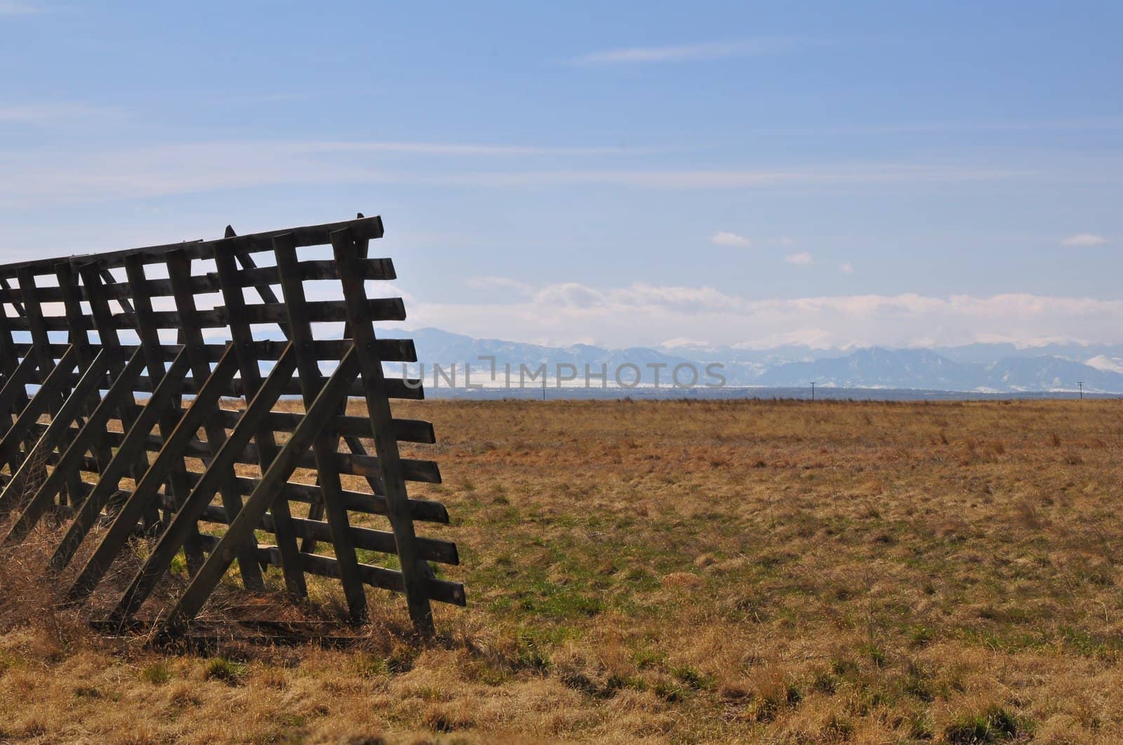 A fence stands in a field with the Rocky Mountains in the distance.