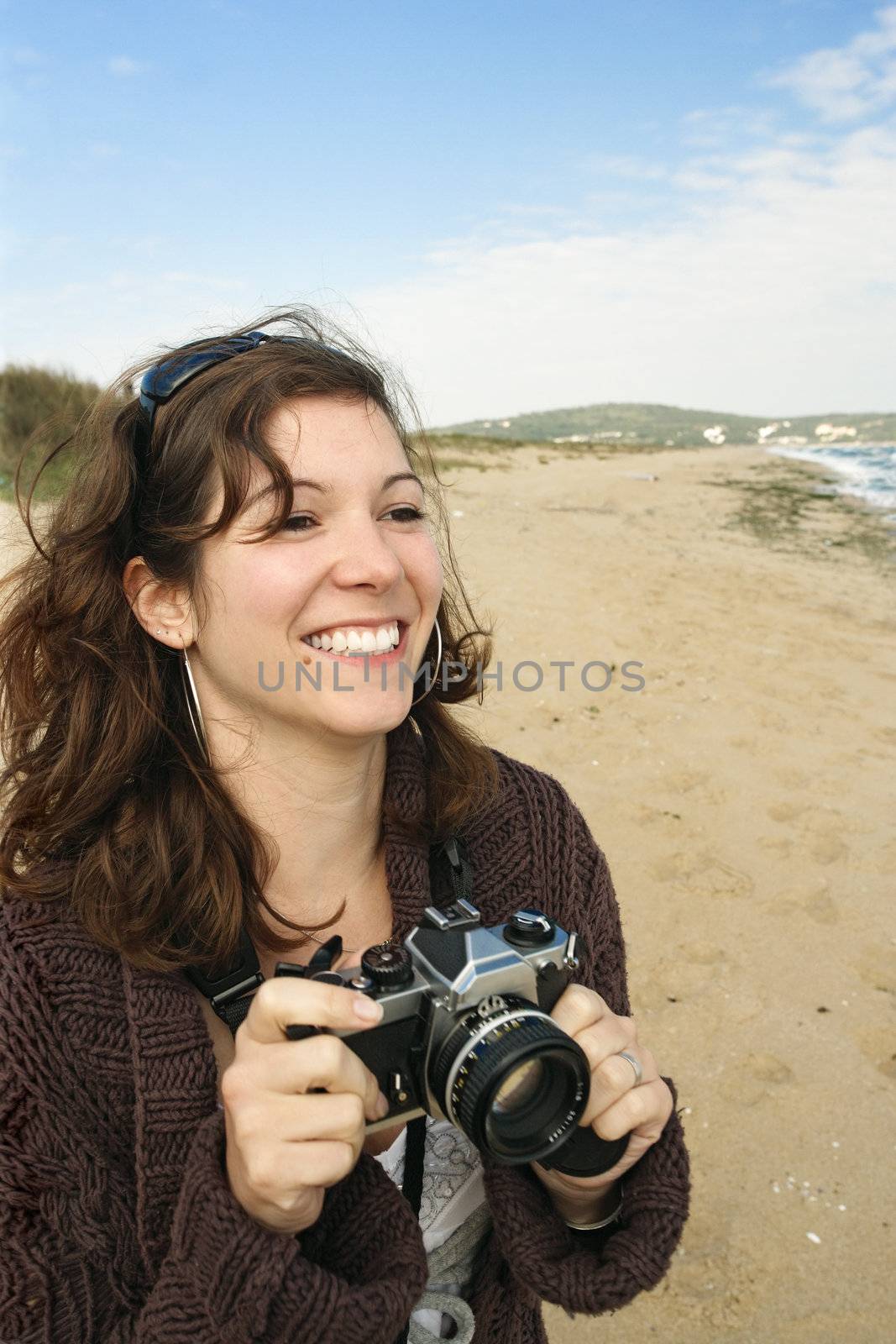 A beautiful young laughing female with an film camera taking holiday pictures at the beach.
