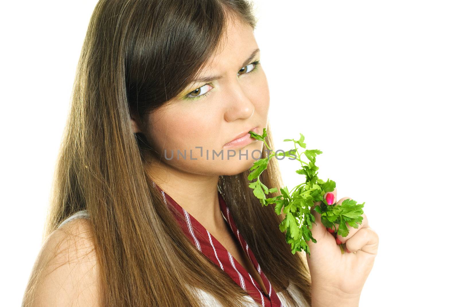 portrait of an unhappy beautiful brunette girl eating fresh green parsley