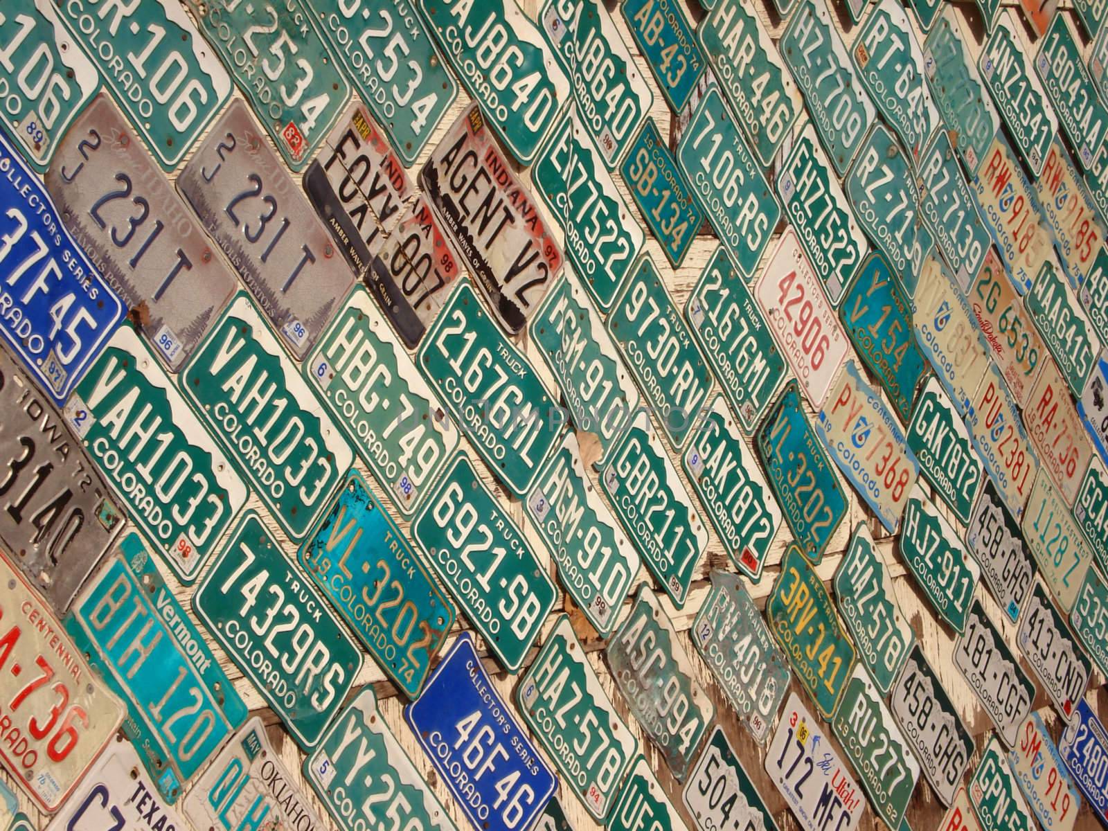 A wall is covered with different color license plates.