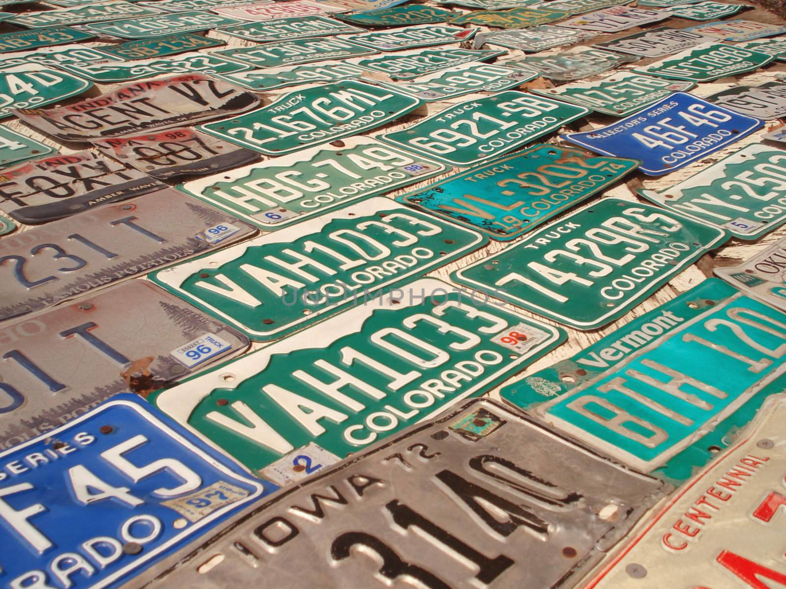 A wall has many different styles of license plates nailed to it.