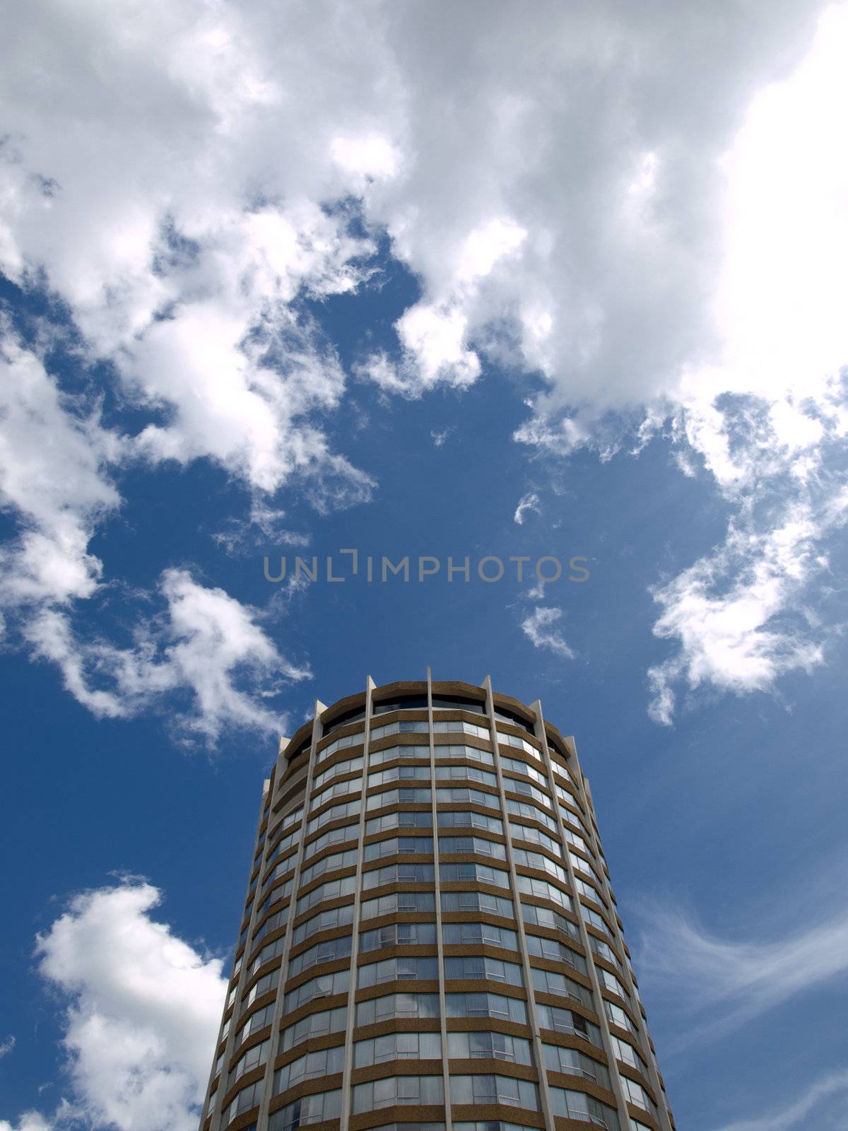 Cylindrical building piercing the cloudy blue sky.