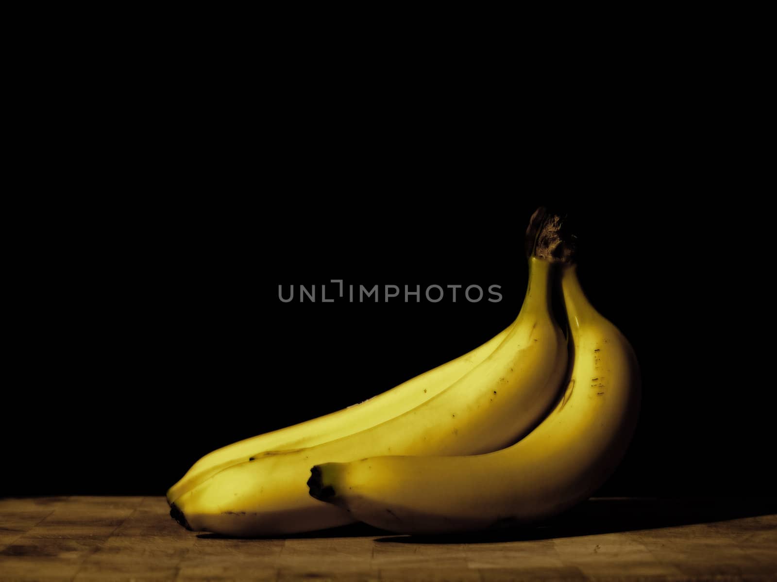 Three fresh bananas on a cutting board shot on a black background.