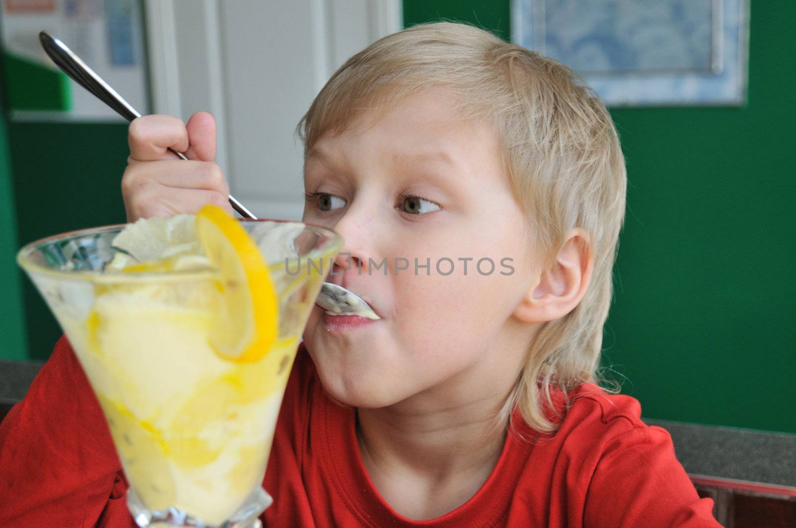 little blondy boy is enjoying his dessert in a cafe