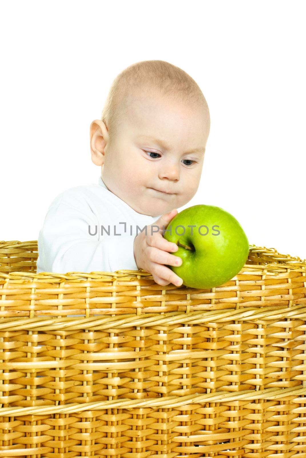 cute six months old baby boy sitting in the basket and holding a green apple