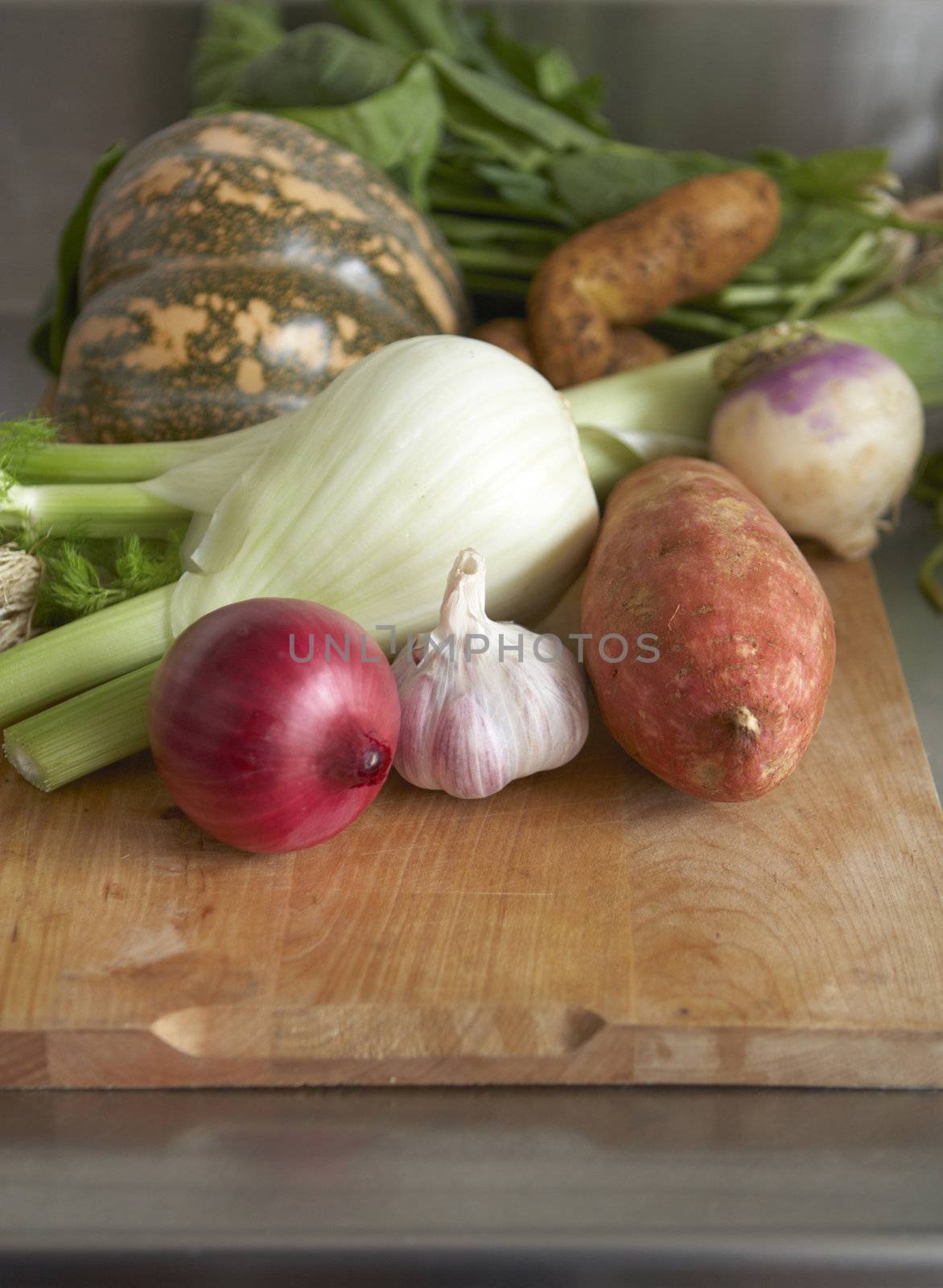 Still life of winter vegetables on wooden chopping board. Stainless steel bench in background