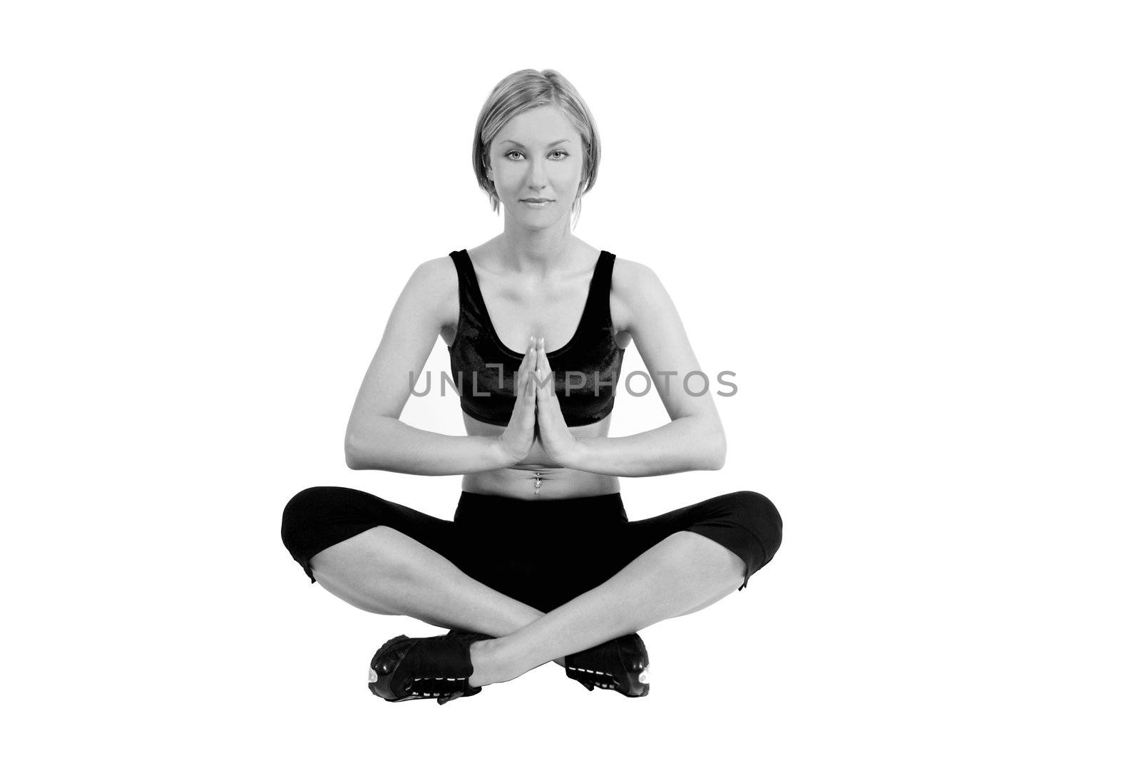 A blond young woman in a fitness outfit is sitting in a lotus position doing yoga. The picture is in B&W.