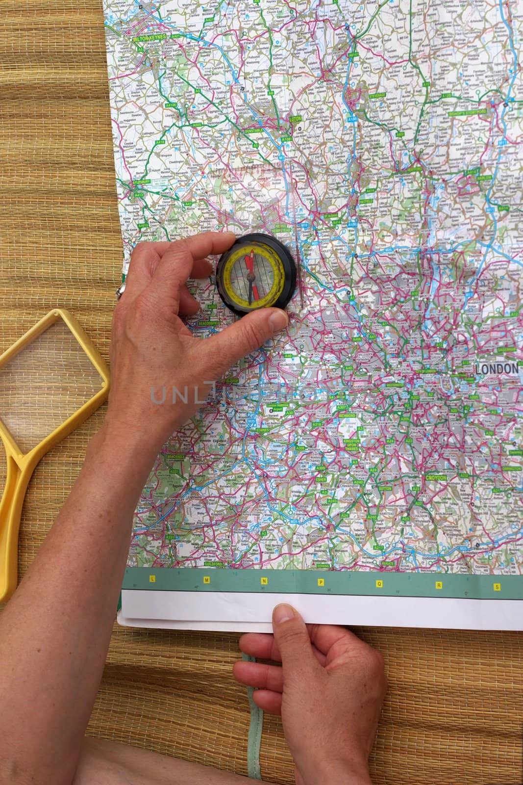 hands of middle aged woman with compass and magnifier glass over map of Greater London, planning next trip