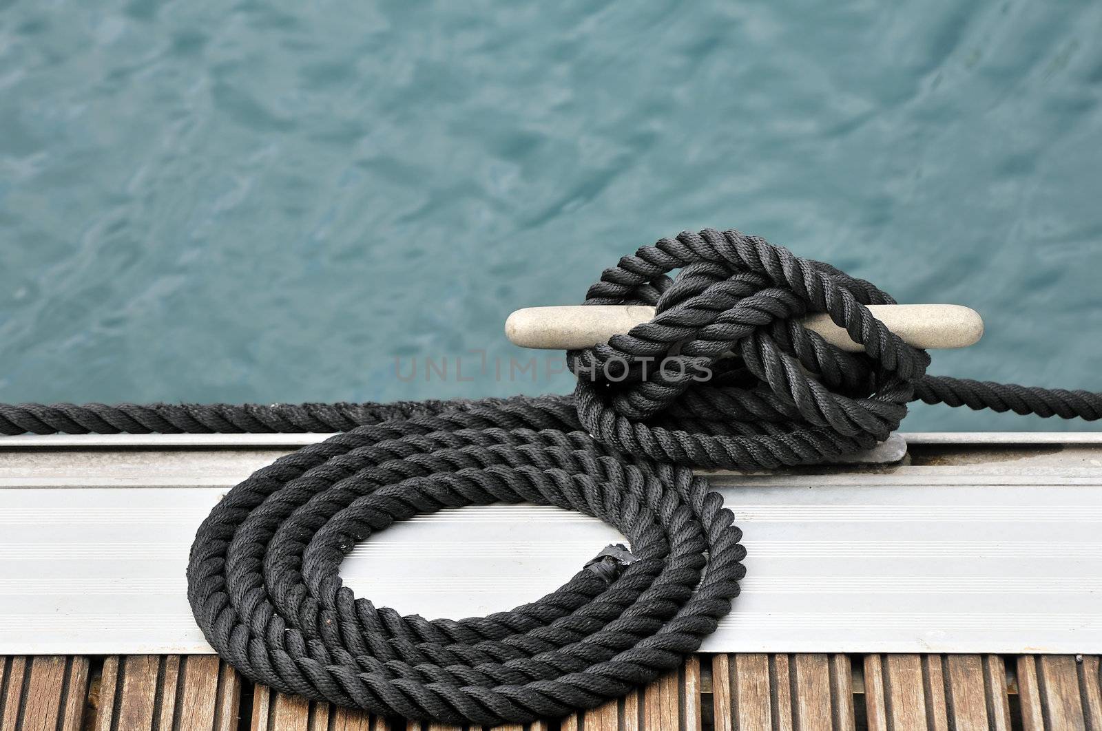 Black rope tied up on a bitt securing boat to jetty