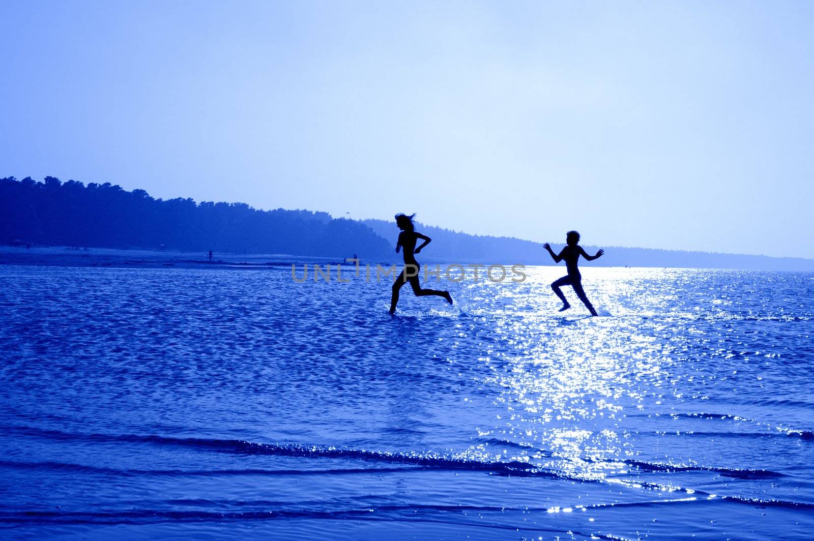 silhouette image of two running girls in water