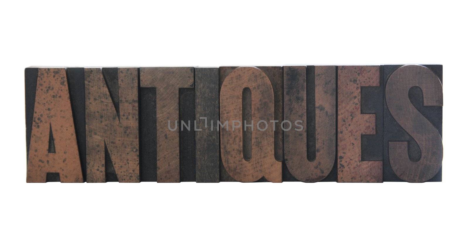 the word 'antiques' in old, ink-stained wood letters isolated on white