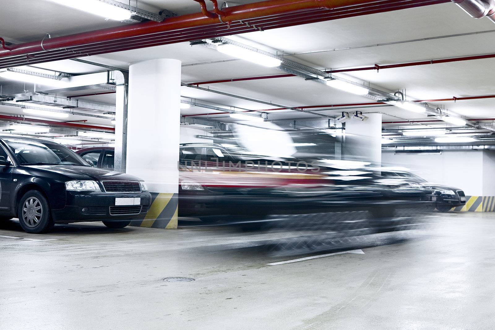 The shined underground garage with the moving cars and parked cars
