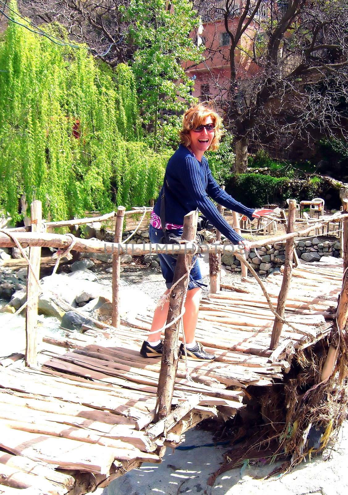 a woman is scared of crossing an unstable bridge over a river.