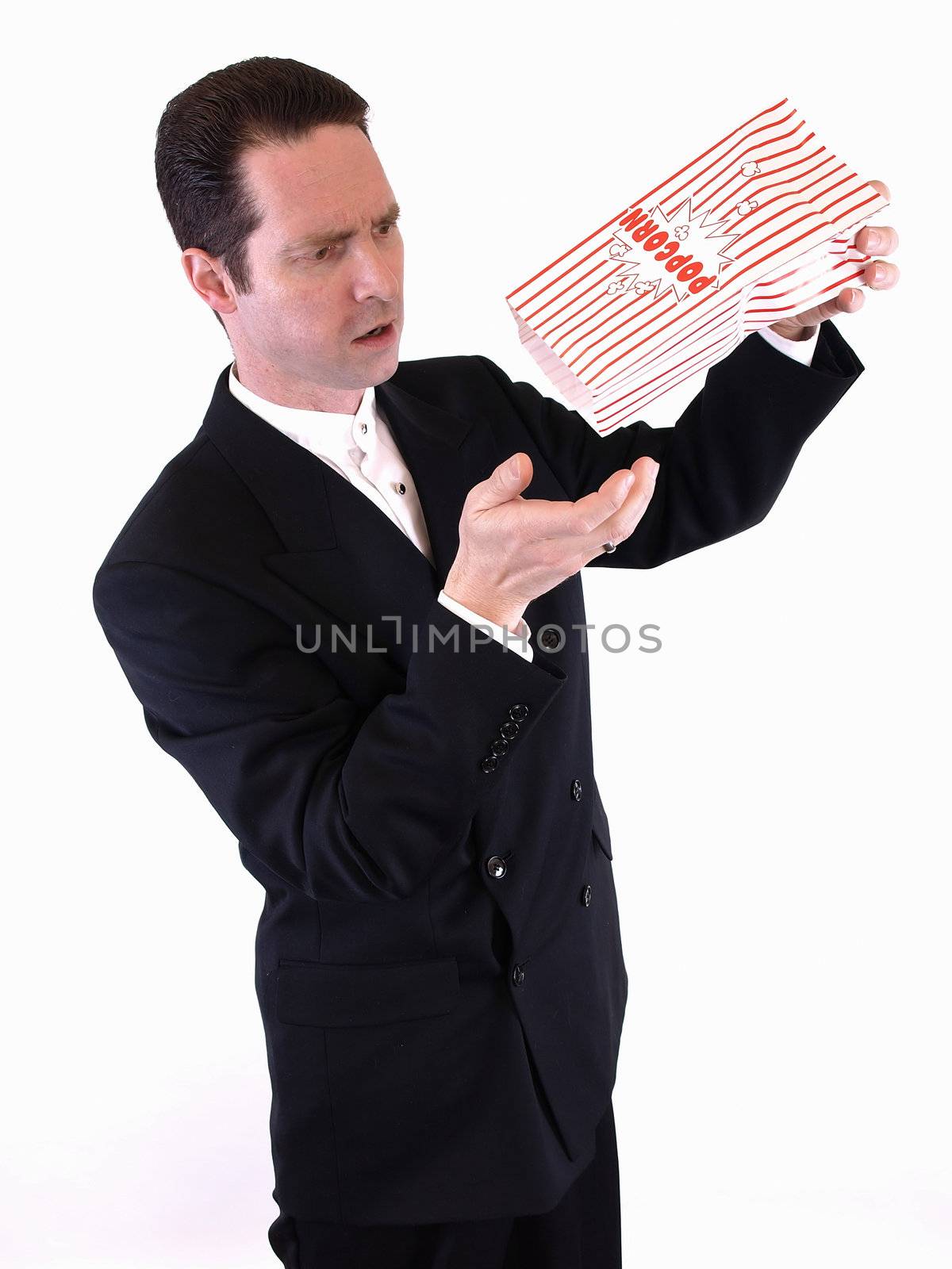 A white male in a suit shakes a bag of popcorn into his hand.  He is frustrated because there is no more.