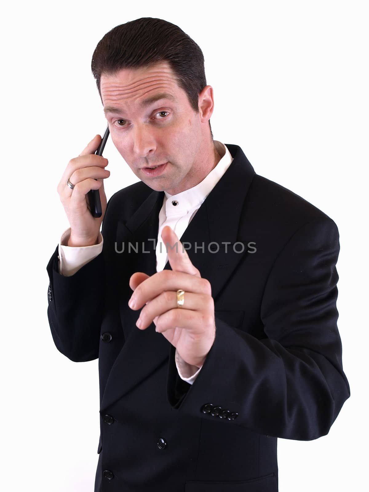 A man in a black suit holds up his finger to signal he is busy and on the telephone.