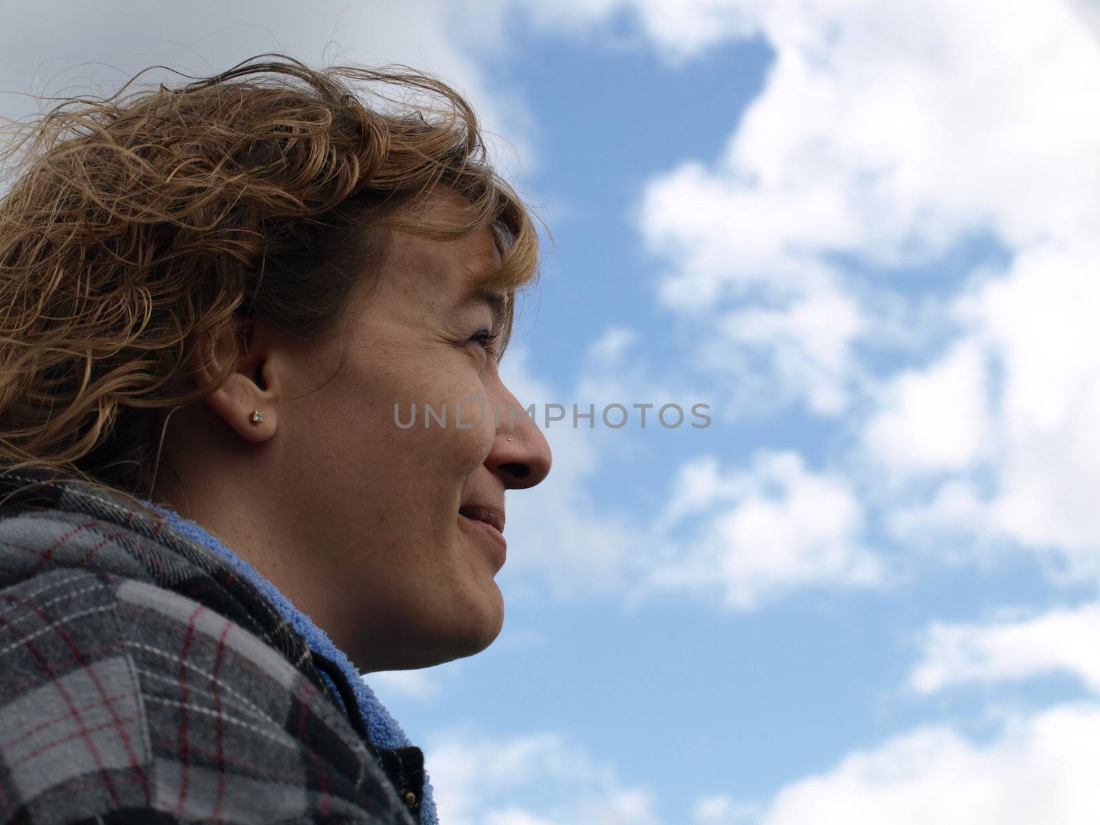 A woman smiles, her back to the gray clouds, looking toward the bright sunny skies.