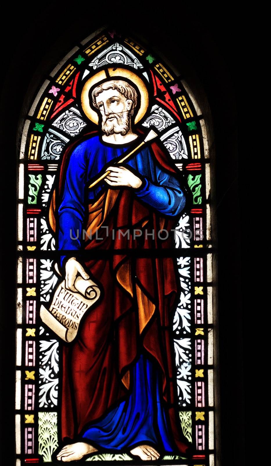 detail of victorian stained glass church window in Fringford depicting St Luke the Evangelist, a scroll in his hands with the beginning of his gospel in latin "Fuit in diebus herodes" 