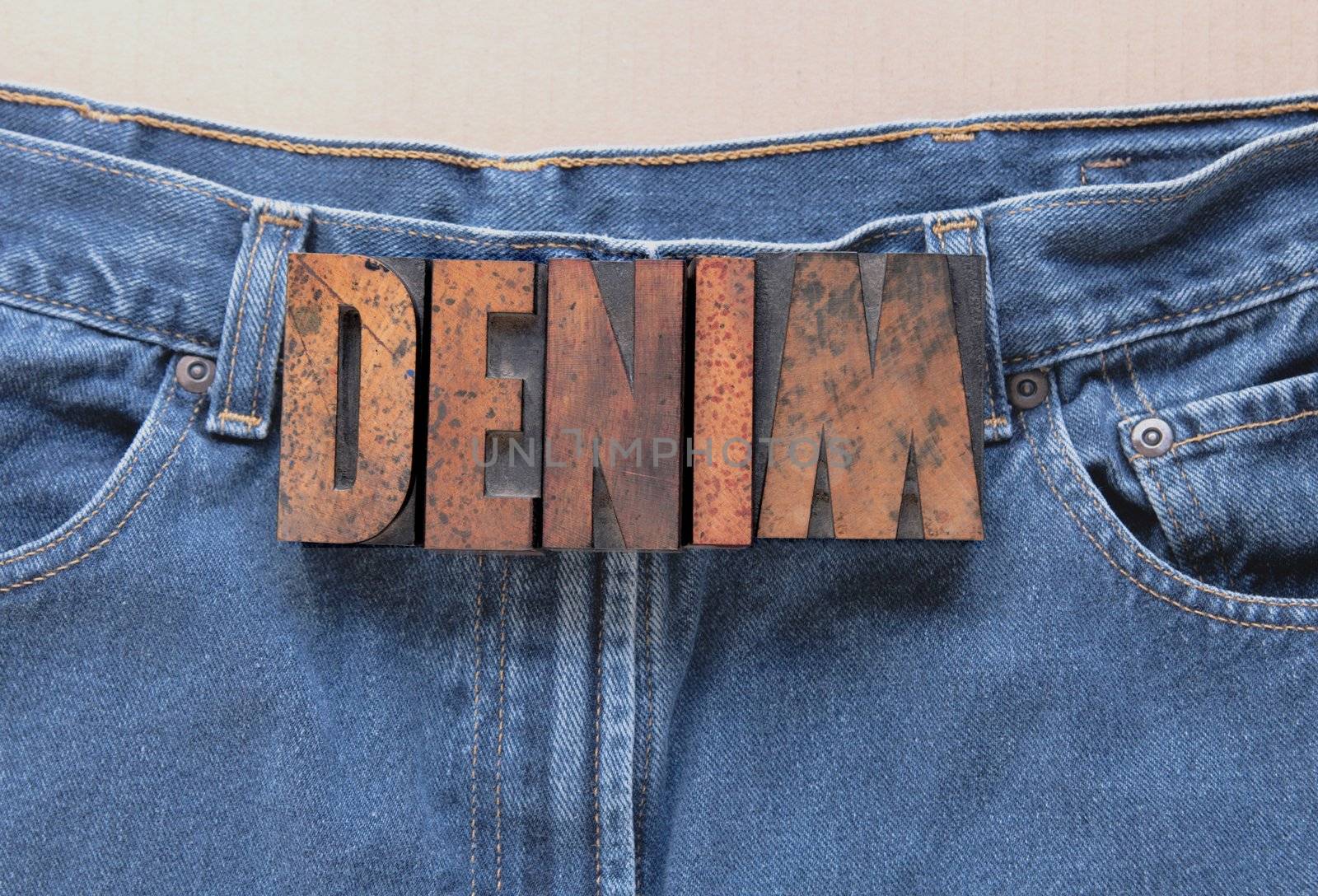 the word 'denim' in wood type on a worn pair of jeans