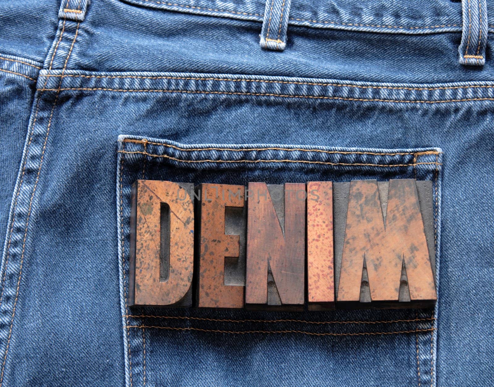 the word 'denim' in wood type on a worn pair of jeans
