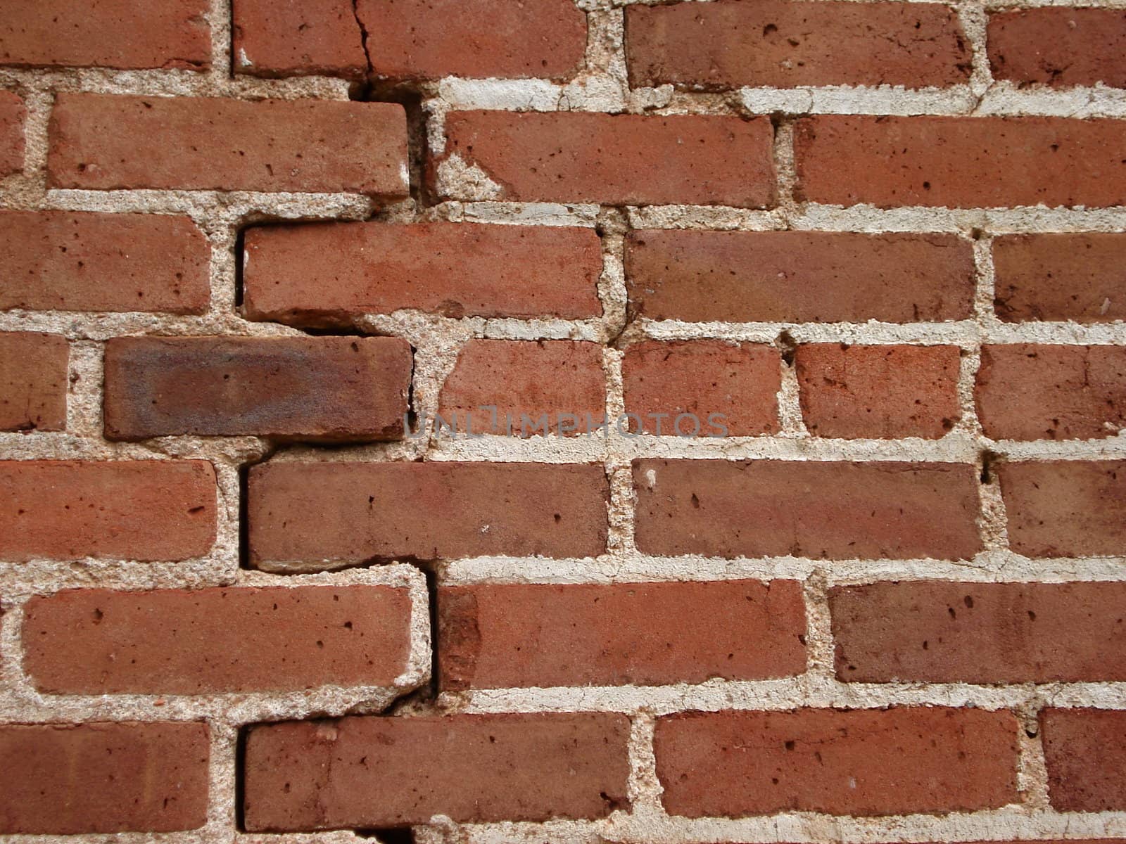 A red brick wall has a vertical crack in it.